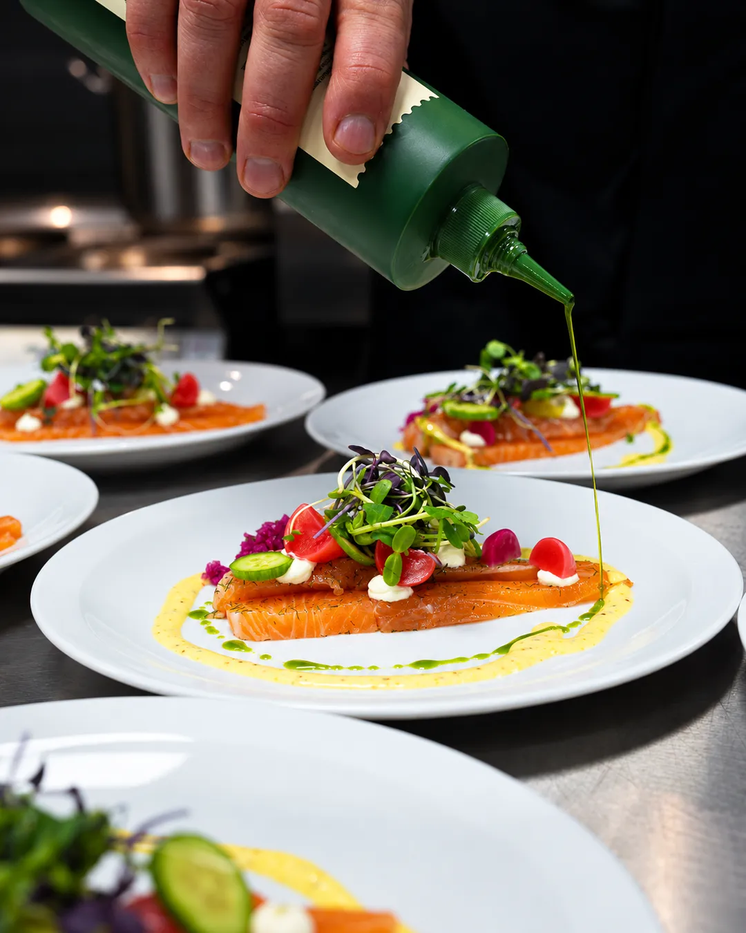 Chef werkt een bord gemarineerde zalm af met kruidenolie