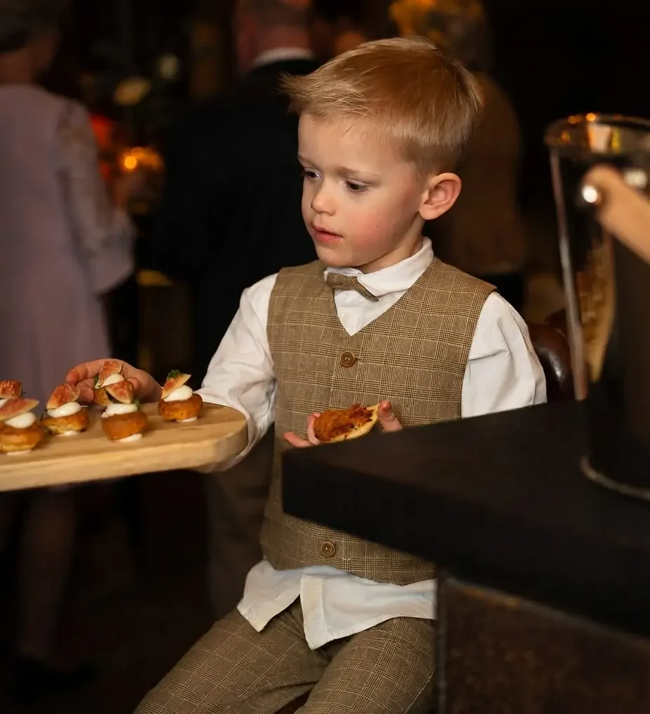 Jongen in gilet serveert hapjes van een plank tijdens een receptie
