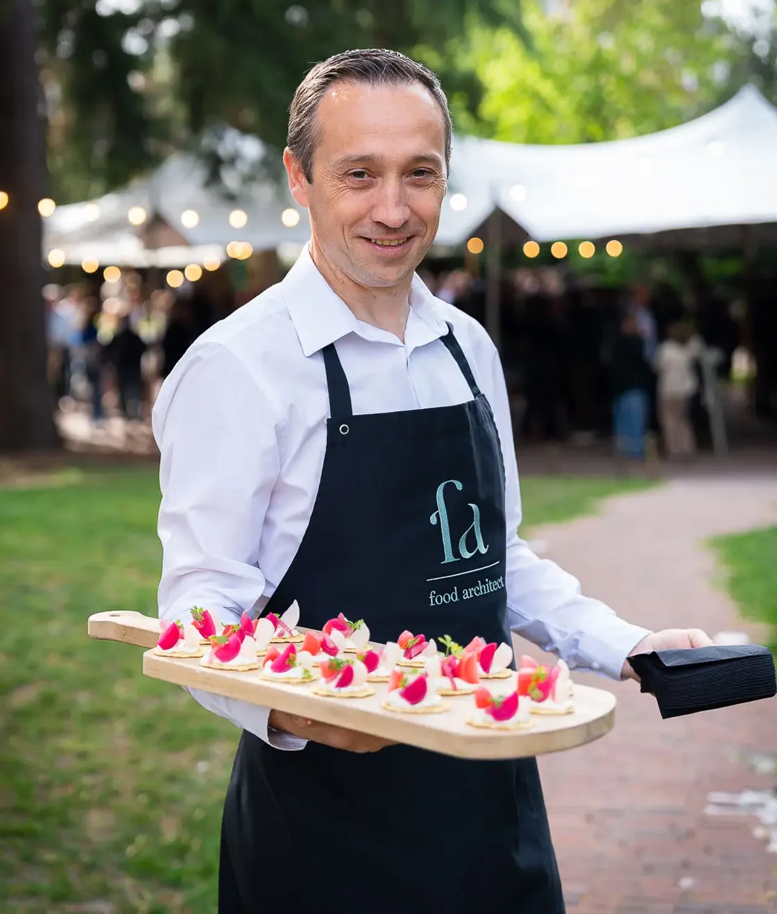 Medewerker met apron van Food Architect draagt een schaal hapjes